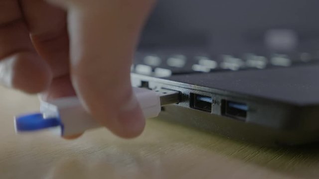 Male hacker stealing information with an usb data stick from a laptop hurrying up and struggling to find the right port to plug it