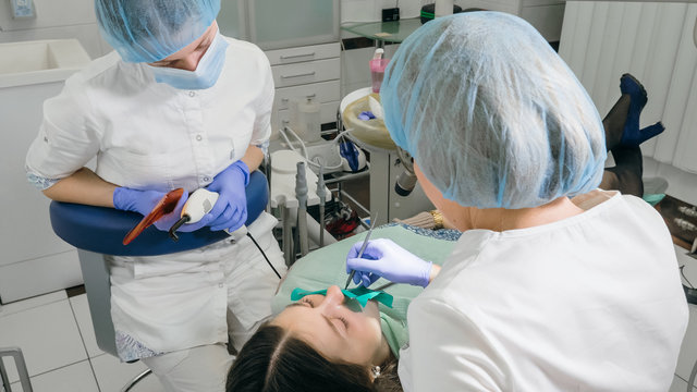 Woman at dentist clinic gets dental treatment to fill a cavity in a tooth. Dental restoration and composite material polymerization with UV light and laser. The doctor works with an assistant.