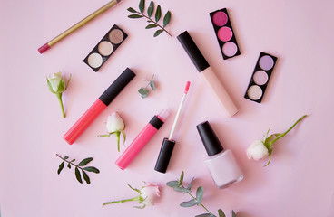 Obraz na płótnie Canvas Lip gloss, nail polish, pencil, eye shadow with flowers on a pink background