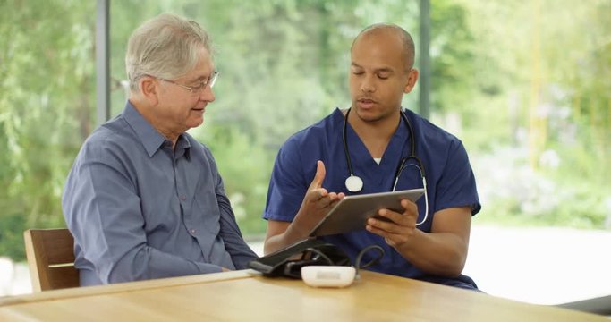 4K Doctor in appointment with elderly man, looking at tablet & discussing test results. Slow motion.
