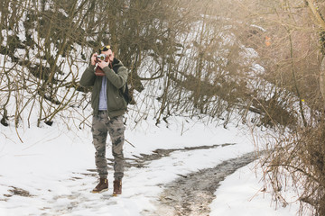 Hipster bearded man with retro camera standing in mountains forest background in winter day