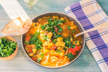 Traditional minestrone soup with pasta and chopped green parsley in a plate on a rustic wooden table close-up with a napkin, sunny day - top view, copy space for a recipe