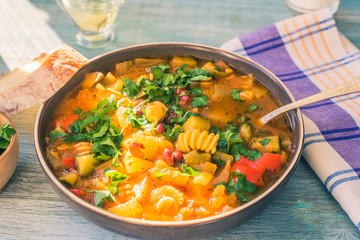 Rustic Italian minestrone soup with pasta and chopped green parsley in a plate on a painted wooden table close-up with a napkin - top view
