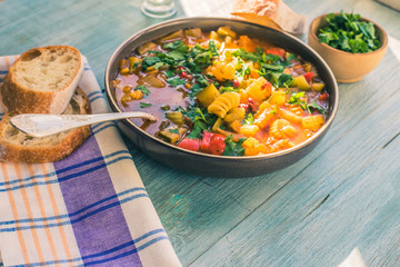 Rustic Italian minestrone soup with pasta and chopped green parsley in a plate on a painted wooden table close-up with a napkin - top view