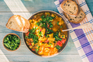 Rustic Italian minestrone soup with pasta and chopped green parsley in a plate on a painted wooden table close-up with a napkin - top view