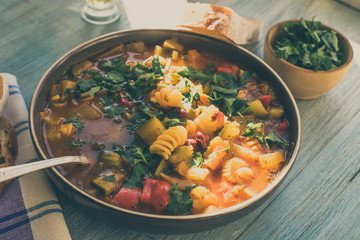 Rustic seasonal minestrone soup with pasta and chopped green parsley in a plate on a painted wooden table close-up with a napkin - top view