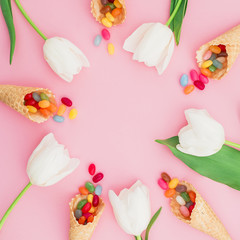 Round frame made of colorful bright candy in waffle cones and tulips flowers on pink background. Flat lay, top view