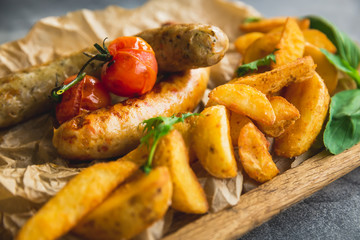 Fried sausages with potatoes and pickled tomato on wooden plate. Tasty food, closeup view.