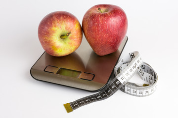 Apple on weight scale and measuring tape with white background