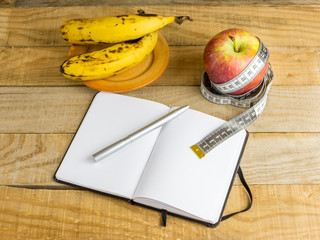 Apple with measuring tape, banana and notebook on wooden table