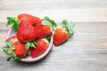 Fresh strawberry in white small dish on wooden background.