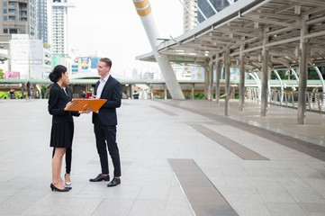 Asian business woman and caucasian businessman holding document file on hand and talk about business future in the city.