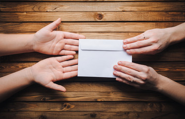 Hands pass the white envelope to the other hands on a wooden background. To send a letter. Transfer of money for donation.