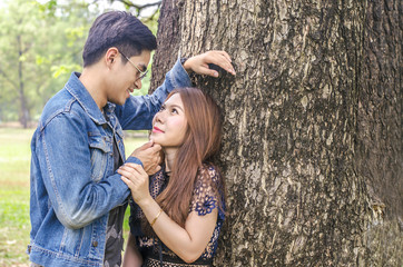 A happy young couple stands near a big tree gently pressing against each other. Love story