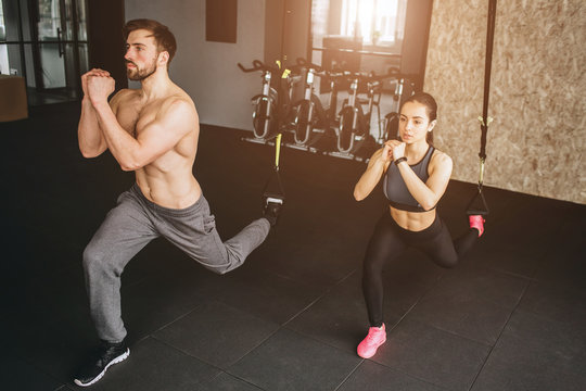 Attractive and slim woman and man are doing lunges on one leg and keeping hands together in front of the body. They are doing this exercise slow but confident.