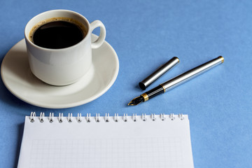 cup of black coffee with notebook  and pen on light blue background. business concept with copy space