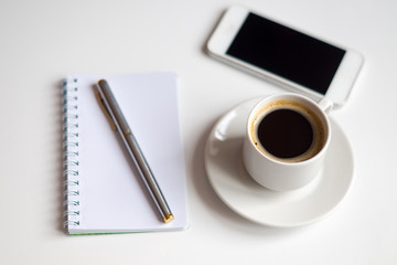 Obraz na płótnie Canvas cup of black coffee, note book, silver pen and white smartphone on white background,