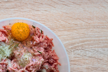 Minced meat in a bowl with raw egg, spices and chopped onion for cooking cutlets, selective focus