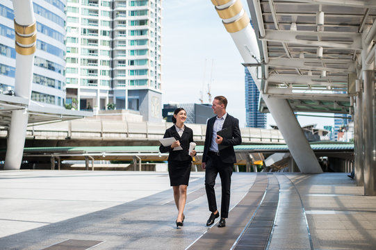 Asian business woman wear suit holding document file on hand and walking together with  Caucasian businessman in the city and talk about business future.