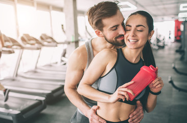 Fototapeta premium Amazing couple standing in the gym. The guy is hugging his girlfriend. She looks happy. Close up. Cut view.