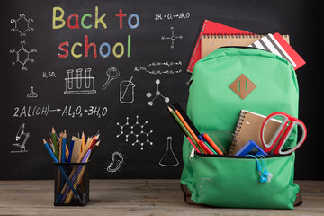 Education concept - school backpack with books and other supplies, blackboard background