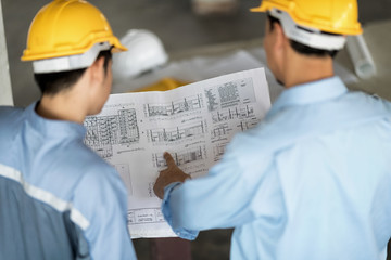 Blueprint in architect's hand. Blur foreground are architect  and engineer in yellow helmet ,they are planning on blueprint. - obrazy, fototapety, plakaty