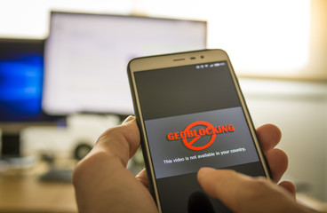 Hands using a smartphone and being unable to navigate online.Geo-blocking concept.