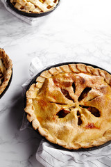 Pie crust design ideas - various ways of pie decoration with lattice and leaves. Apple, strawberry and raspberry pies cooked and served with tea on white marble table