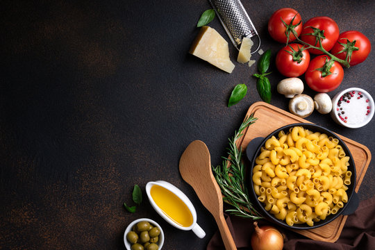 Pasta and ingredients for cooking on dark background, top view. Italian food concept. Pasta, tomatoes, basil, vegetables and spices. Copy space