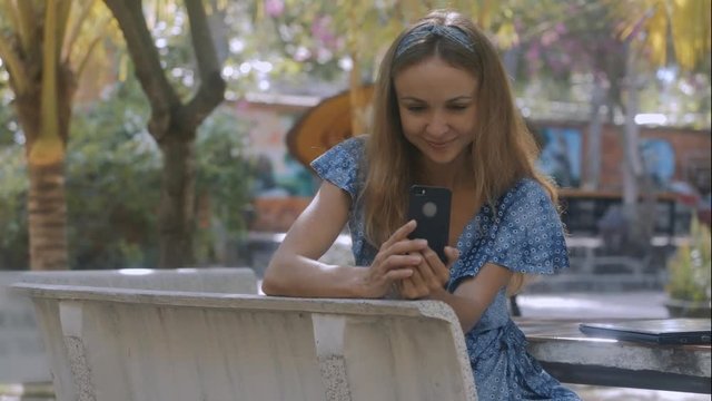 Pretty Girl Reads Sms on IPhone on Stone Bench in Park
