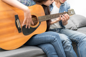 In selective focus of Young beautiful couple resting at home and playing guitar.Woman learning to playing a song.