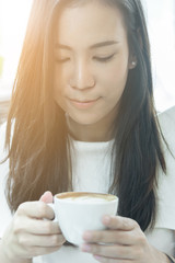 Beautiful asian attractive woman has holding and drinking a coffee at coffee cafe in the morning with happy and relaxing time.
