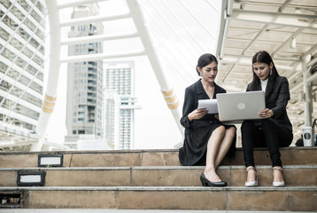 Fototapeta premium two business women sit on the staircase and talk about business with laptop and copy space for text
