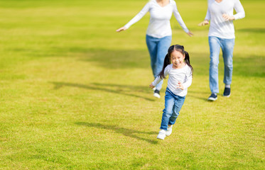 Little girl is running with parents in the park. Young family with little kid having fun in nature.