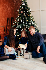 young mother and father and their little daughter in a New Year decor with gifts and a Christmas tree