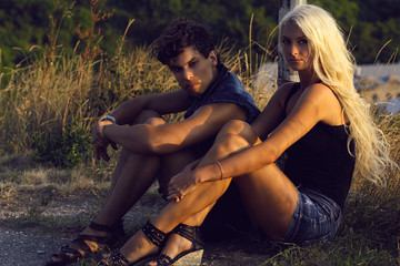 A beautiful girl and a guy are sitting on a rock together, at sunset