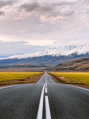 Inspirational travel and adventure photography. Straight paved road with white surface markings goes through the snow capped mountains of Altai Republic, Russia just before the sunset.