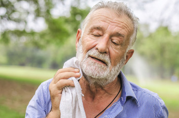 Senior man wiping sweat of his  with towel in park - obrazy, fototapety, plakaty