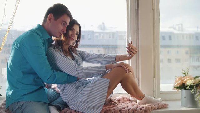 Happy cheerful loving couple making selfie on window, young attractive guy and girl