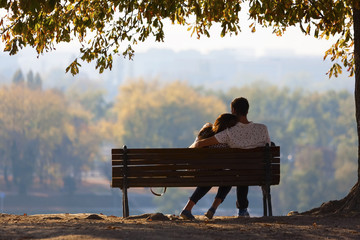 Young couple sitting on a wooden bench under a tree. Kalemegdan park in Belgrade  - obrazy, fototapety, plakaty