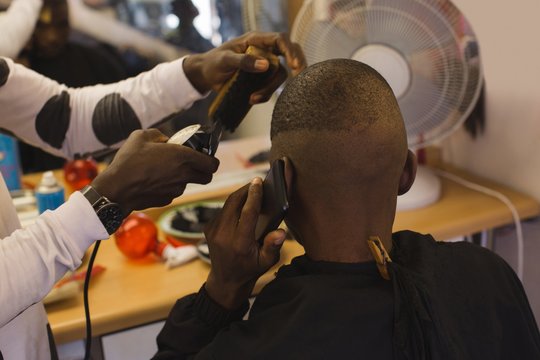 Customer talking on mobile phone while barber trimming his hair