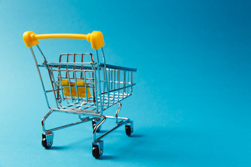 Close up of supermarket grocery push cart for shopping with black wheels and yellow plastic elements on handle isolated on blue background. Concept of shopping. Copy space for advertisement