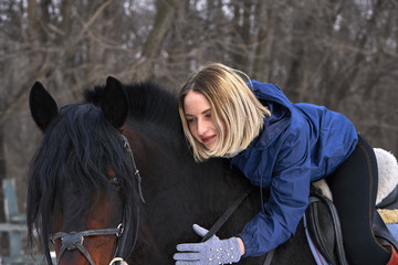 A young girl with white hair is riding a horse. The girl hugs her favorite horse. Winter cloudy...