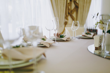 Beautiful decoration of a wedding banquet in a restaurant in pastel colors. Serving the table with beige tablecloth, plates, glasses, cutlery, napkins decoration with a green twig