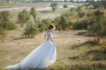 Beautiful wedding photosession. Young charming bride in white lace dress with long plume and...