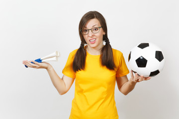 European young sad upset woman, two fun pony tails, football fan or player in glasses, yellow uniform hold football pipe, ball isolated on white background. Sport, play football, lifestyle concept.