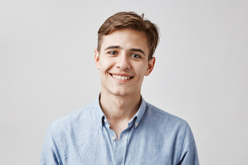 Cute boy with brown hair and beautiful smile standing next to the wall. His birthday is today so coworkers made surprise party. Guy looks happy he did not expected they will remember. - obrazy, fototapety, plakaty