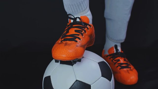 Footballer in boots putting his leg on a ball, black background