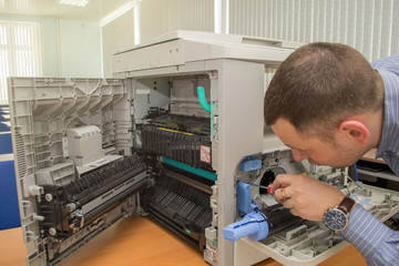 young male technician repairing using a screwdriver and a brush digital photocopier machine