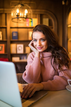Beautiful young woman using laptop at cafe while drinking coffee at break time